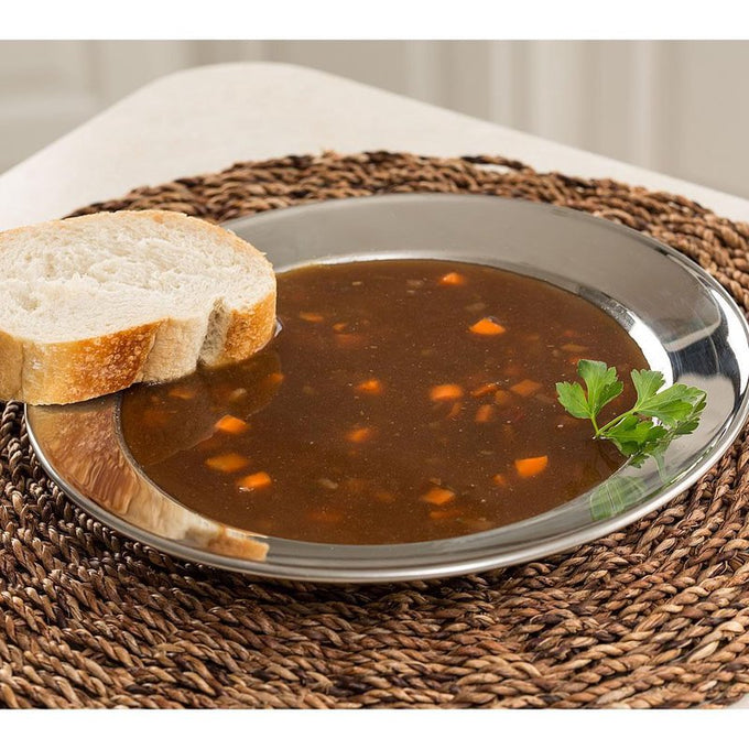 Handcrafted stainless steel soup plate with a wide rim holding vegetable beef soup and a slice of bread, styled on a woven placemat for Kitchen & Food, Dinnerware, and Best Sellers collections.