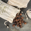 Small brown soap nuts spilling from a natural cotton drawstring bag onto a stone surface, accompanied by textured beige cloths, showcasing an organic and eco-friendly laundry supply.