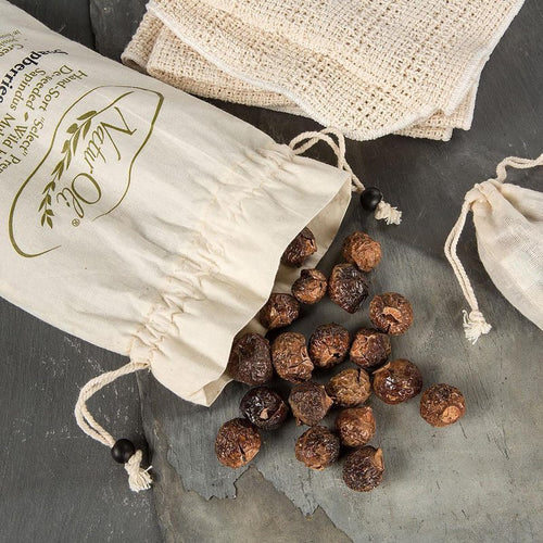 Small brown soap nuts spilling from a natural cotton drawstring bag onto a stone surface, accompanied by textured beige cloths, showcasing an organic and eco-friendly laundry supply.