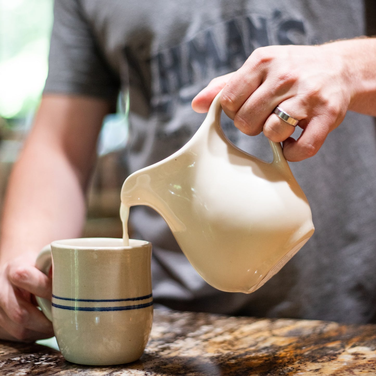 Handcrafted cream stoneware pitcher pouring liquid into a blue-striped ceramic mug, made in the USA, featured in Kitchen & Food, Dinnerware, Storage and Serving, USA Made, and Best Sellers collections.