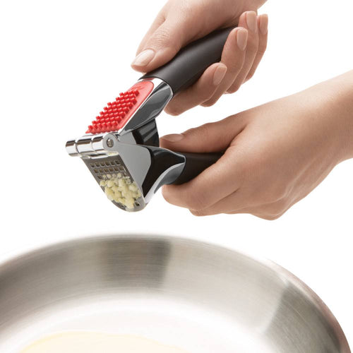 Garlic press with soft non-slip black handles and a large stainless steel crushing chamber, shown pressing garlic cloves over a metal pan, part of Kitchen & Food and Cooking and Baking Helpers collections.