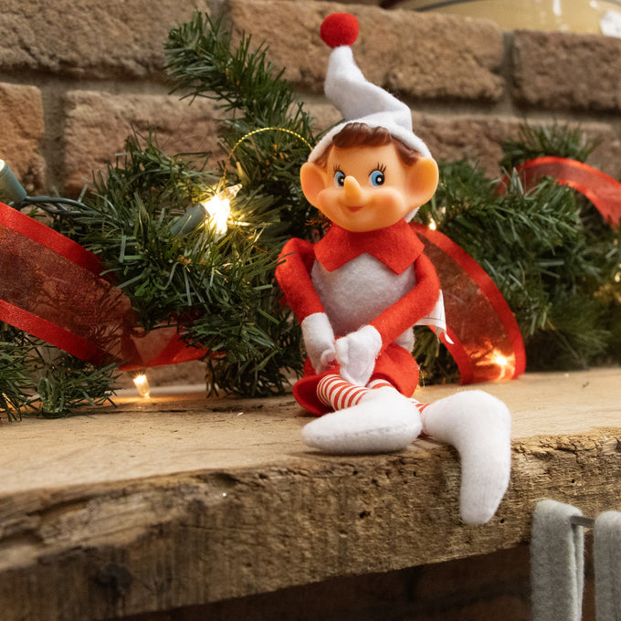 Posable vintage-style Christmas pixie elf ornament in red and white fabric with striped tights and a festive pom-pom hat, displayed on a rustic wooden mantel with holiday greenery and lights, ideal for Home & Decor and Holiday Decor collections.