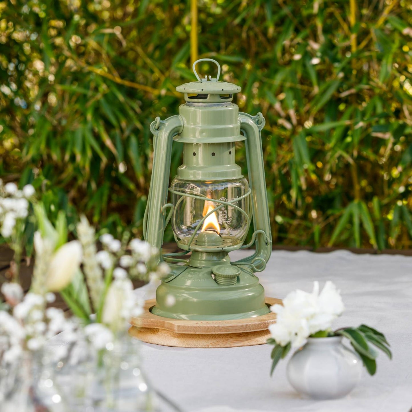Handcrafted pale green Feuerhand Galvanized Oil Lantern with thermal heat-resistant SUPRAX globe, softly glowing on a wooden base outdoors, ideal for Lamps & Lighting, Camping, Emergency Supplies collections.
