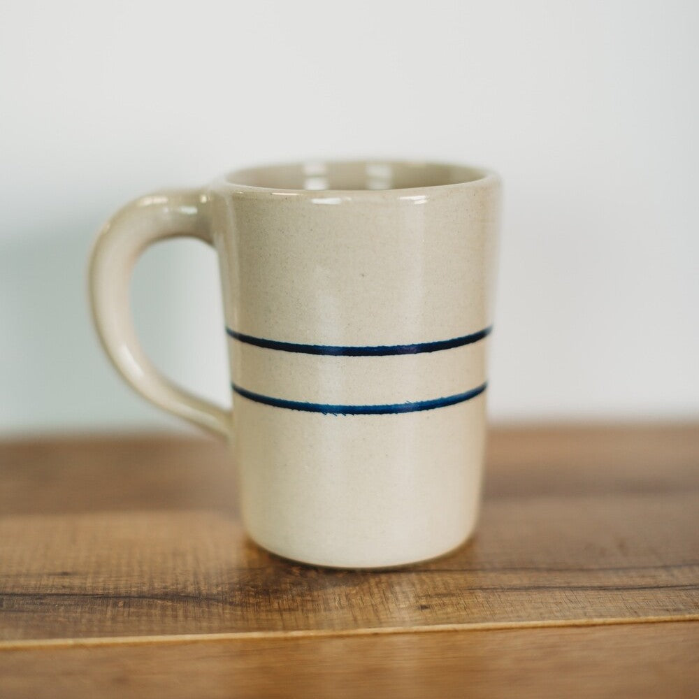 Handcrafted tall stoneware mug with a natural beige color and two blue stripes, designed for brewing coffee and tea, perfect for kitchen and dinnerware collections in the USA made category.