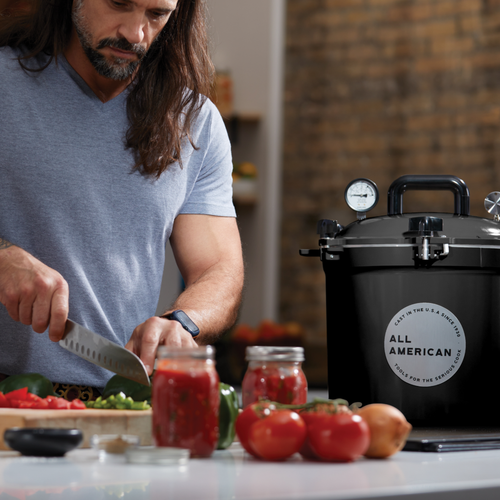 Glossy black pressure canner with secure locking lid and pressure gauge beside a man chopping fresh vegetables for food preservation in Kitchen & Food, Canning, and USA Made collections.