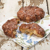 Two glazed fruit fritters, one whole and one broken to show fried fruit chunks inside, resting on a floral napkin on a rustic wooden surface, handcrafted and made in USA, ideal for Kitchen & Food, Snacks and Sweets, Holiday Hosting, USA Made, Best Sellers, Promo Eligible collections.