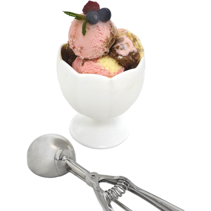 Stainless steel scoop with spring handle resting next to a white ceramic dessert cup filled with three scoops of ice cream garnished with fresh berries, handcrafted for Kitchen & Food, Cookware, Baking Supplies, Kitchen Gadgets, and Best Sellers collections.