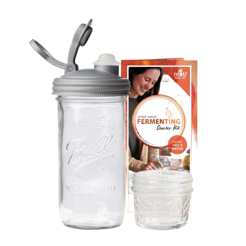 Clear wide-mouth glass jar with a gray fermentation lid and waterless airlock next to a small Mason jar and instructional packaging, ideal for kitchen fermenting and food preservation, USA made.