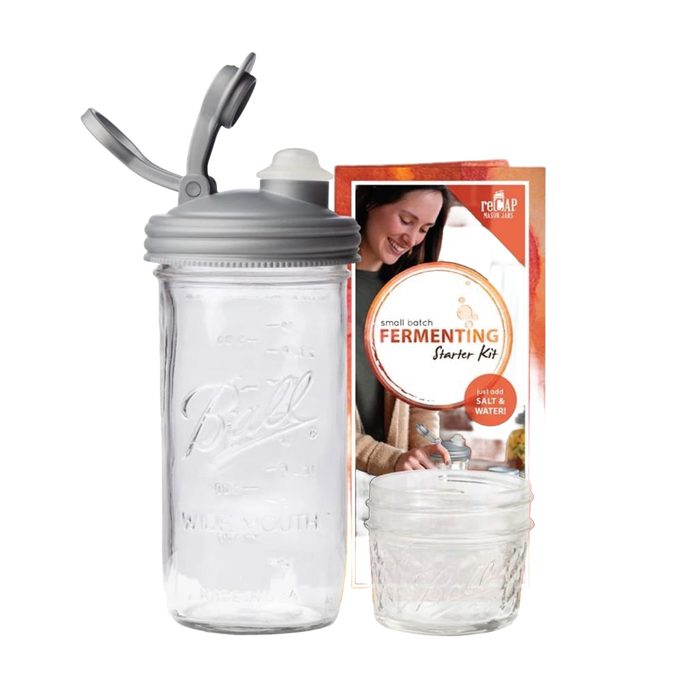 Clear wide-mouth glass jar with a gray fermentation lid and waterless airlock next to a small Mason jar and instructional packaging, ideal for kitchen fermenting and food preservation, USA made.