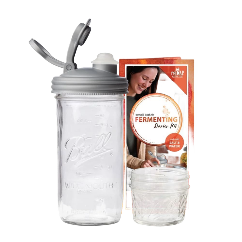 Clear wide-mouth glass jar with a gray fermentation lid and waterless airlock next to a small Mason jar and instructional packaging, ideal for kitchen fermenting and food preservation, USA made.