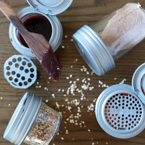 Set of four airtight spice shaker lids for regular-mouth jars with flip tops and shaker inserts, shown with various spices and a wooden spreader, ideal for Kitchen & Food, USA Made, and Cooking Helpers collections.