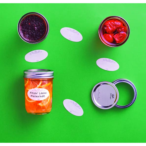 Set of dissolvable oval labels with decorative borders displayed alongside jars of homemade preserves and canning lids on a bright green background, suited for Kitchen & Food, Food Preservation, Canning Accessories, USA Made, and Best Sellers collections.