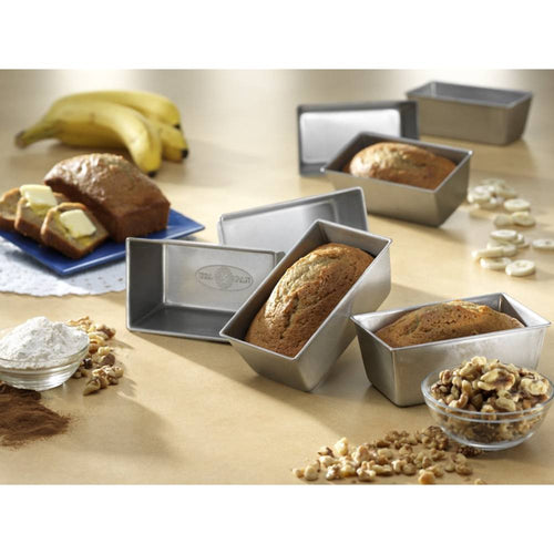 Set of four handcrafted mini loaf pans made in USA arranged with freshly baked bread, surrounded by baking ingredients in a warm kitchen setting, featured in cookware and baking supplies collections.