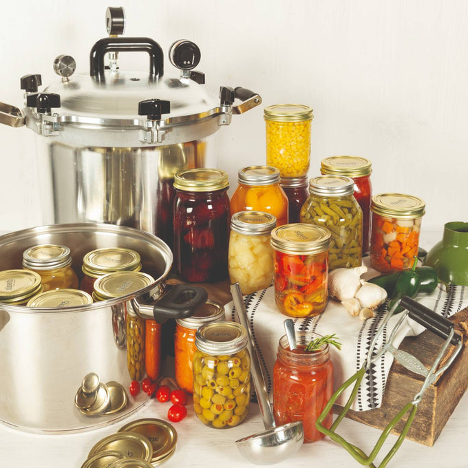 Assortment of home-canned vegetables and fruits sealed in glass jars with gold-tone lids, arranged alongside a stainless steel pressure canner and cooking pot, featured in Kitchen & Food, Food Preservation, and Canning collections.