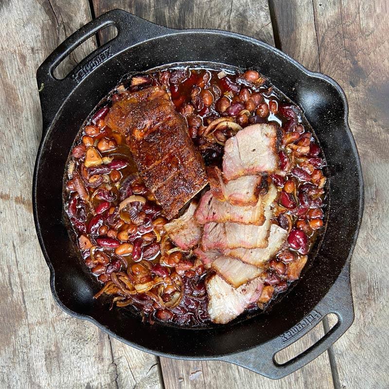 Handcrafted cast iron skillet with two side handles cooking a hearty dish of slow-cooked beans and sliced smoked meat, ideal for farm, kitchen, camping, cookware, and cast iron collections.