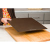 Hand holding a slim, dark baking steel above a wooden cutting board in a kitchen setting, ideal for Kitchen & Food, Cookware, Baking Supplies, and Bread Making collections.