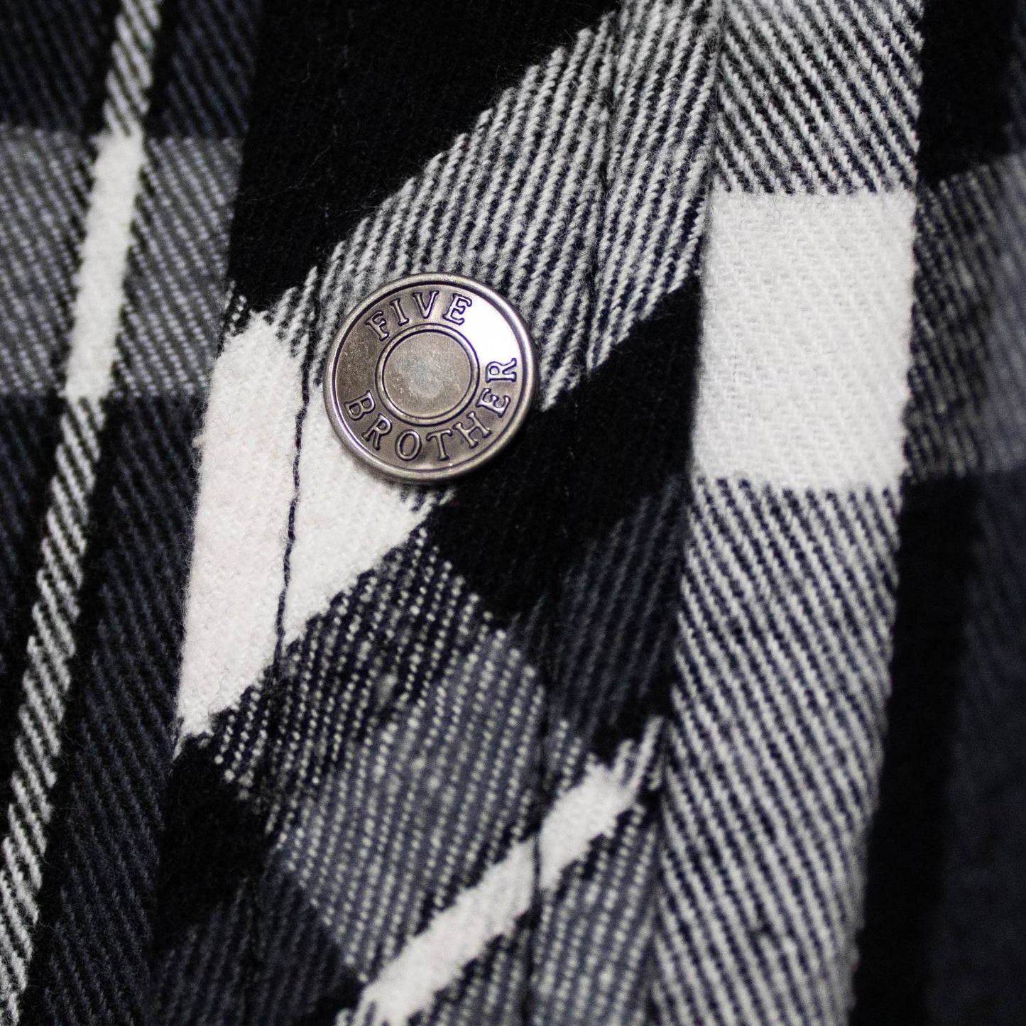 Close-up of handcrafted black and white plaid flannel fabric with detailed texture and metal snap button engraved with "FIVE BROTHER," featured in Health & Wellness and Clothing and Accessories collections.
