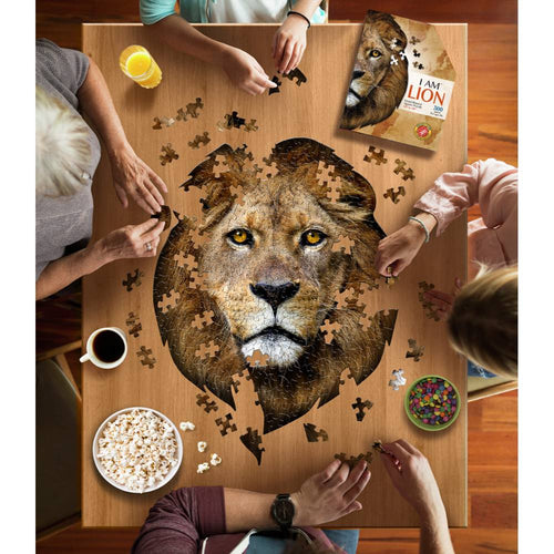 Group of four people assembling a uniquely shaped jigsaw puzzle of a lion's face on a wooden table, surrounded by snacks and beverages, part of children's toys and puzzles collections.