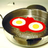 Red high heat resistant silicone double egg poacher with two eggs cooking simultaneously in a stainless steel skillet, ideal for kitchen gadgets and cooking helpers collections.