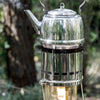 Shiny stainless steel kettle steaming on a portable cooking attachment for outdoor camping in a natural forest setting, part of Farm, Garden & Tool and Camping collections.