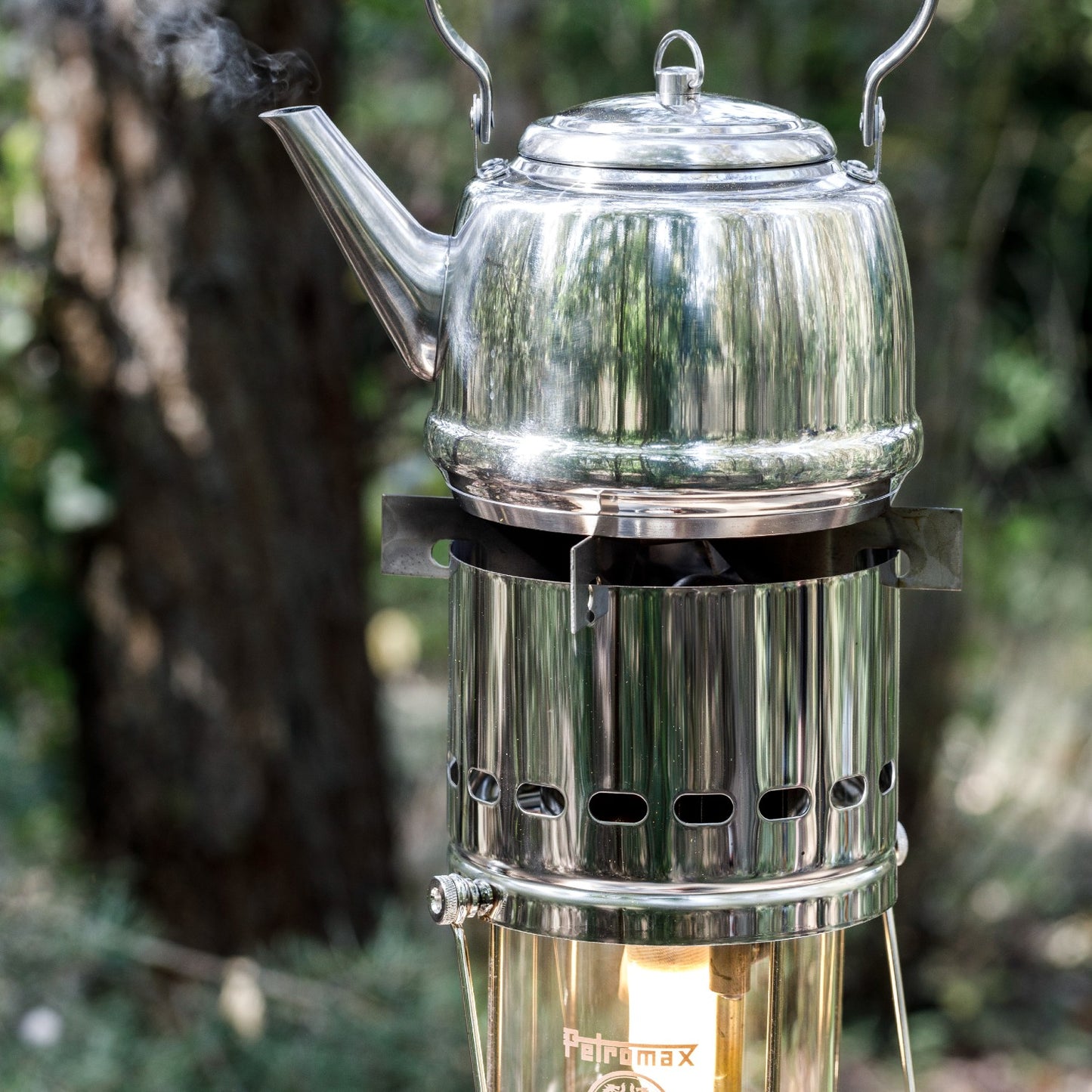 Shiny stainless steel kettle steaming on a portable cooking attachment for outdoor camping in a natural forest setting, part of Farm, Garden & Tool and Camping collections.