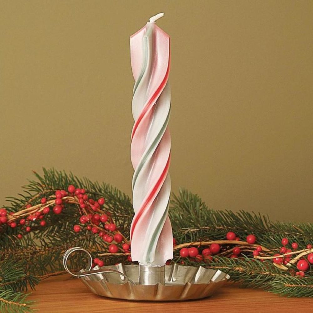 Hand-dipped spiral candle with red and green twists standing in a vintage metal holder, surrounded by festive holiday greenery and red berry accents, perfect for seasonal decor.