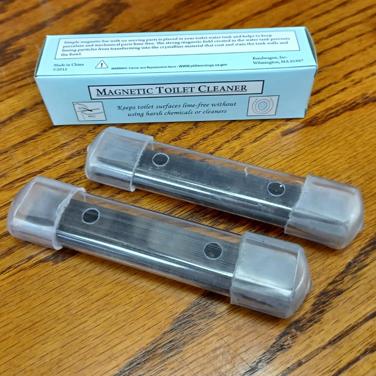 Two clear plastic housings containing long-lasting magnets designed to prevent mineral buildup and stains in toilet tanks, shown with a labeled box on a wooden surface, part of Home & Decor and Household Cleaning collections.