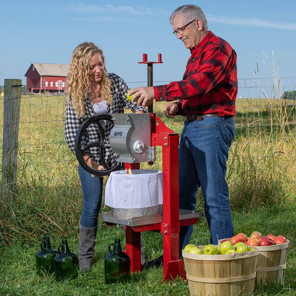 Man and woman using a handcrafted red-framed stainless steel cider press with black hand crank in orchard setting, part of Farm, Garden & Tool and Apple Harvest Supplies collections.