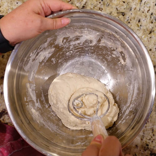Handcrafted Old Country dough whisk with a wooden handle and two spiral metal wires stirring dough in a stainless steel bowl, part of Kitchen & Food, Baking Supplies, and Amish Made collections.