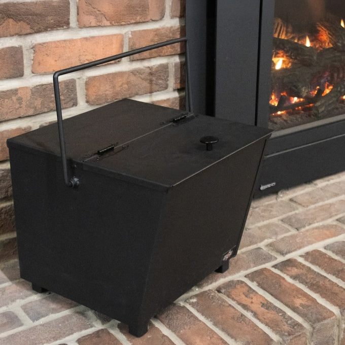 Heavy-duty black steel ash carrier bucket with a balanced handle and legs, designed for safe ash cleanup near a fireplace, made in the USA, ideal for stoves and hearth accessories collections.