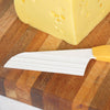 Soft cheese knife with a uniquely drafted white resin blade and comfortable yellow handle resting on a wood cutting board beside a block of semi-soft cheese, handcrafted and made in the USA, ideal for Kitchen & Food and Food Prep collections.
