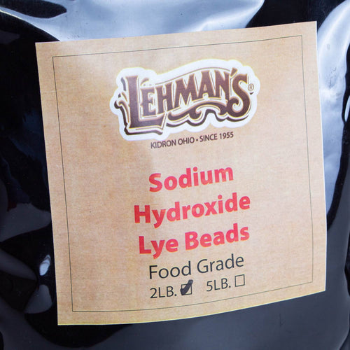 Close-up of a resealable black bag featuring a kraft paper label with Lehman's logo and red text indicating food-grade sodium hydroxide lye beads available in 2-lb or 5-lb sizes, part of health and wellness and soapmaking supplies collections.