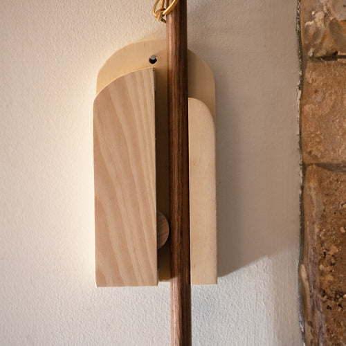 Handcrafted Amish-made wooden wall-mount broom holder with a sliding ball mechanism, mounted beside a stone wall, ideal for Home & Decor, Household Helpers, Cleaning Utensils, USA Made, and Best Sellers collections.