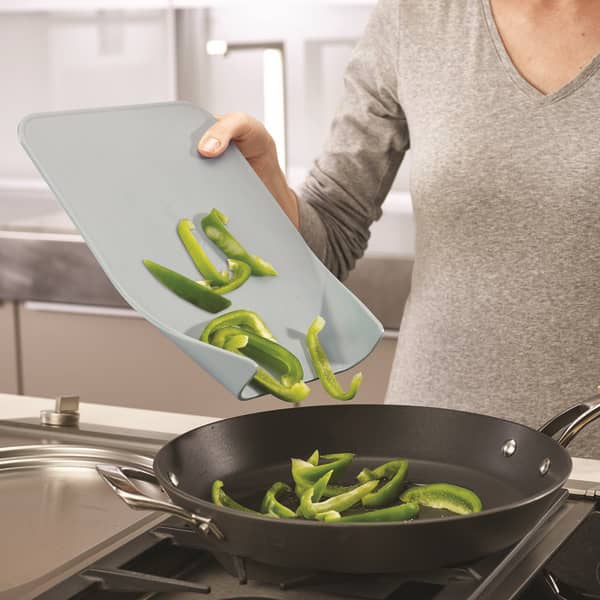Person using a compact, space-saving chopping board with easy-pour ends to transfer sliced green bell peppers into a black frying pan, ideal for Kitchen & Food and Food Prep collections.