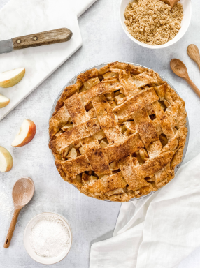 Golden brown lattice apple pie baked in a 9-inch aluminized steel pan with fluted surface, surrounded by baking ingredients and utensils, ideal for Kitchen & Food and Baking Supplies collections.
