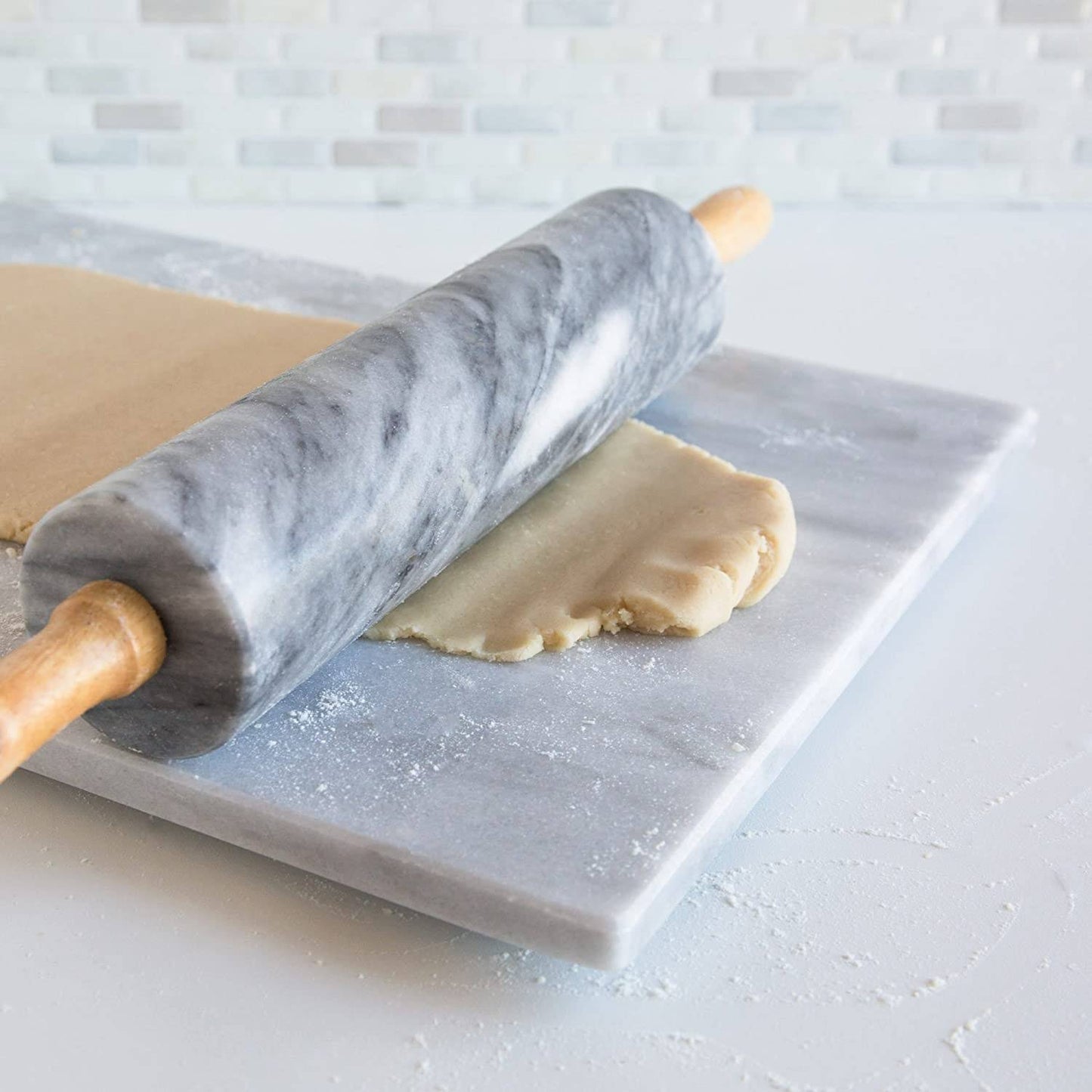 Marble rolling pin with wooden handles resting on a matching marble board, rolling out dough in a bright kitchen setting, featured in Kitchen & Food and Baking Supplies collections.
