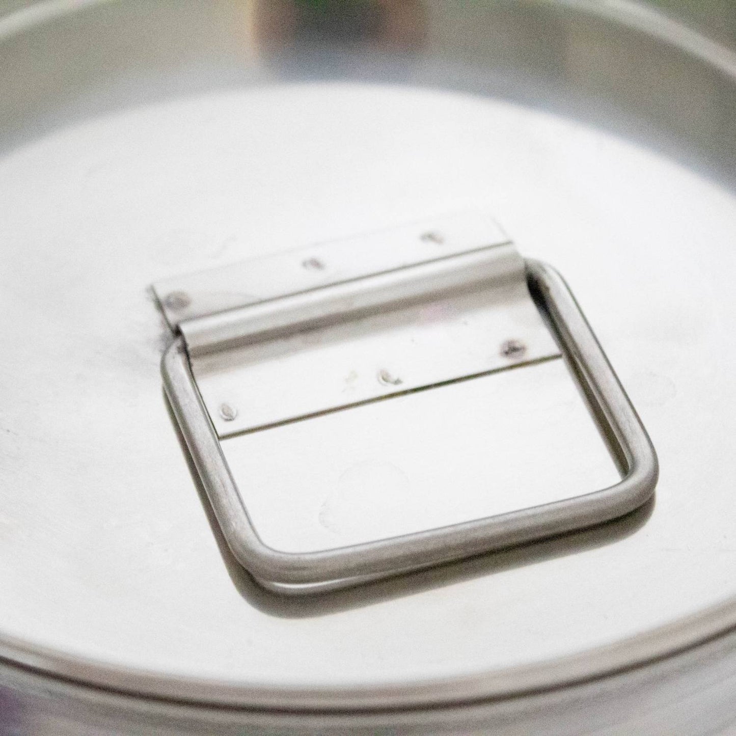 Close-up of a sturdy stainless steel handle attached to the seamless lid of a small milk can, crafted from durable 304 grade steel for use in farm, garden, and animal care settings.