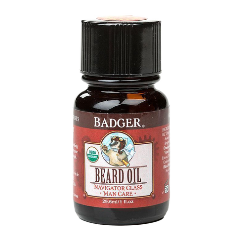 Dark amber glass bottle with black cap containing handcrafted beard oil, featuring an illustrated badger logo and red label, made in USA for grooming and personal care.