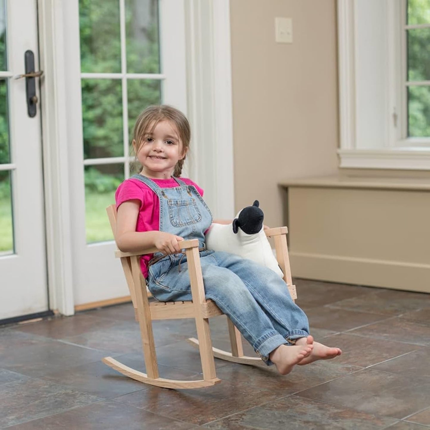 Young child sitting barefoot in a handcrafted wooden rocker made of unfinished solid oak, holding a stuffed animal indoors, showcasing exclusive Amish-made quality for Toys, Books & Games and USA Made collections.