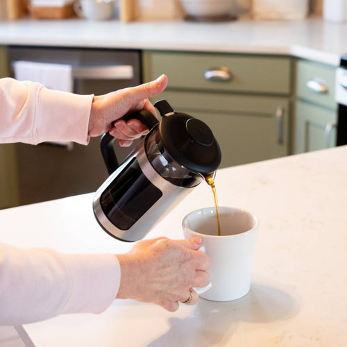 Pouring coffee from a stainless steel framed French press with black lid and handle into a white mug on a kitchen countertop, featured in Kitchen & Food, Brewing Coffee and Tea, Best Sellers, and Promo Eligible collections.