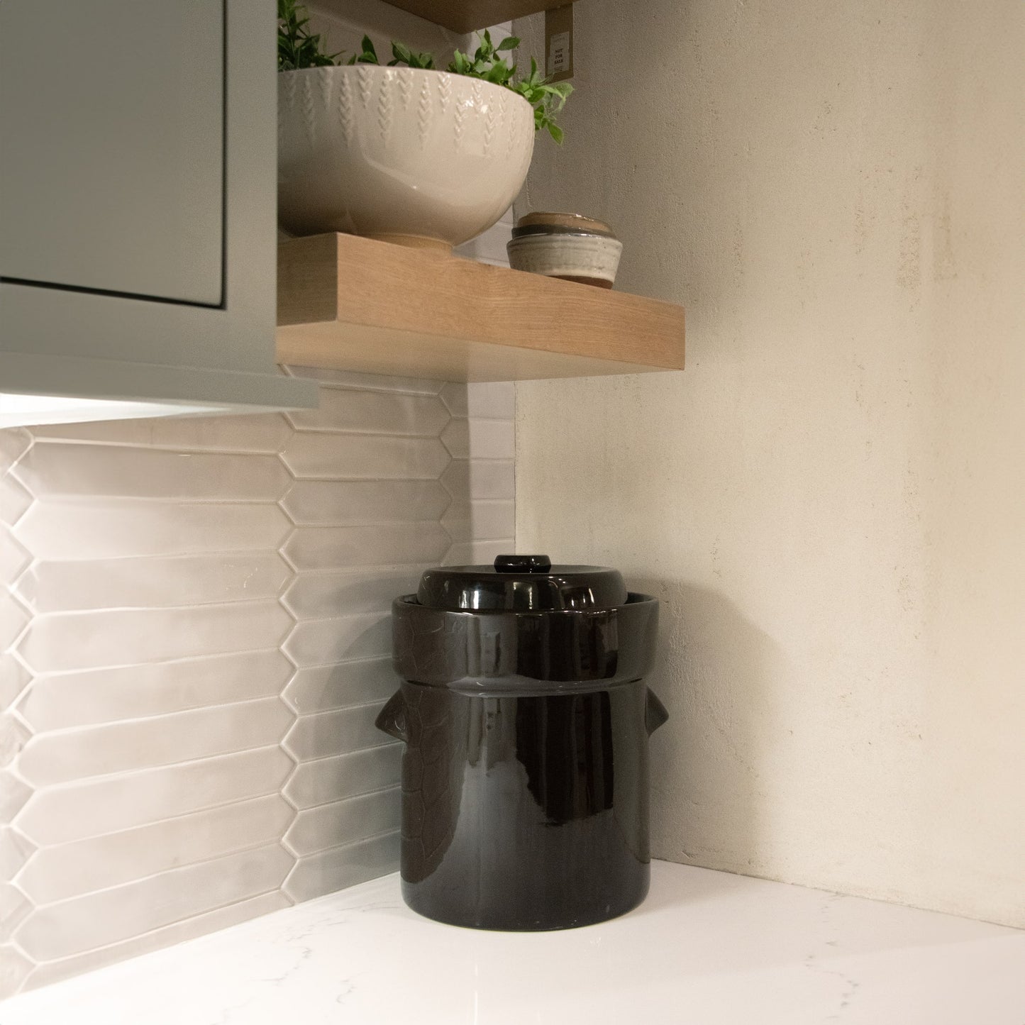 Handcrafted black stoneware fermenting crock with lid, placed on a white kitchen countertop under a wooden shelf, ideal for Kitchen & Food, Food Preservation, Fermenting and Pickling, Best Sellers, and Promo Eligible collections.