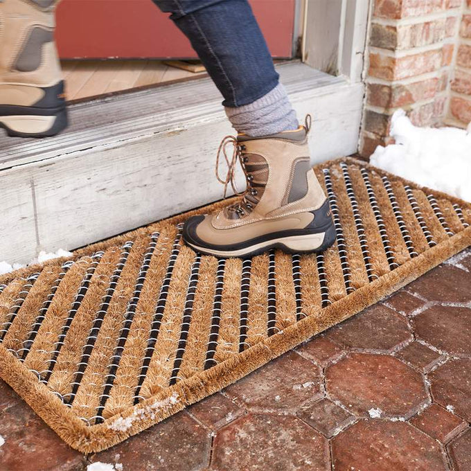 Person stepping onto a sturdy bootscraper rug with natural coconut fibers and wire brushes, designed for heavy-duty dirt removal, part of Home & Decor and Best Sellers collections.