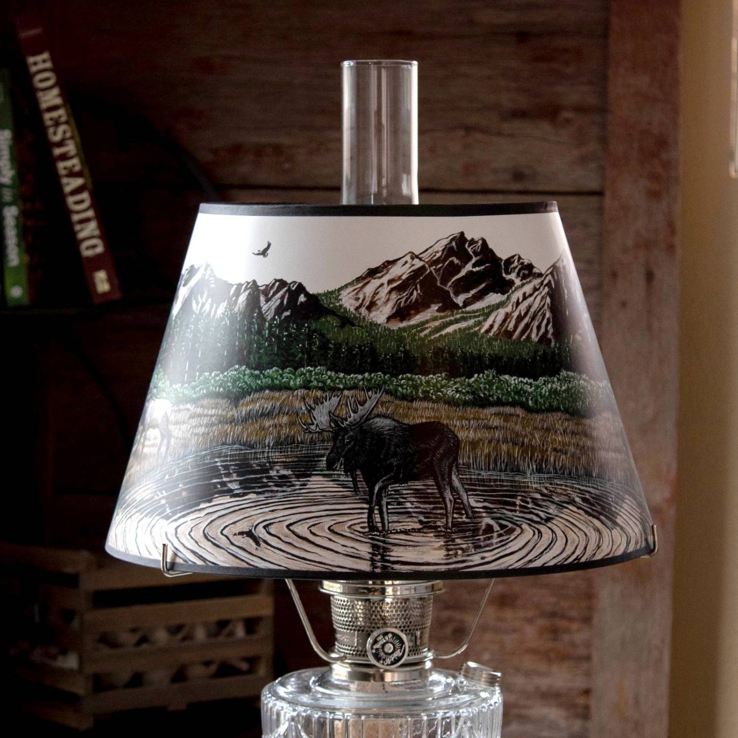 Clear oil lamp with brass burner and a parchment shade featuring a moose wading in water with forest and mountain landscape, ideal for Lamps & Lighting, Oil Lamps, Table Lamps, Best Sellers, Promo Eligible collections.