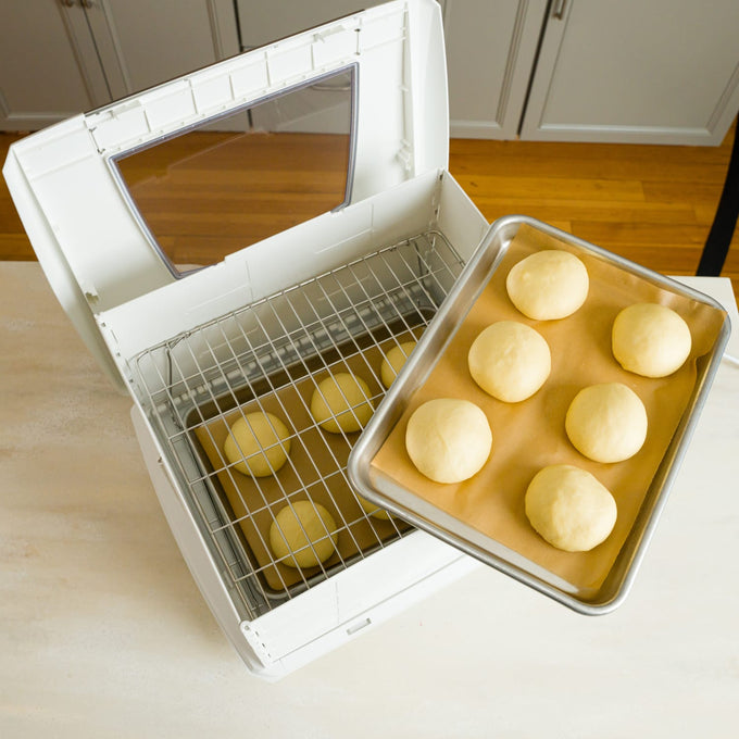 White folding bread proofer with clear lid open, showing metal rack inside and a tray of six smooth dough balls on parchment, ideal for precise rising in Kitchen & Food and Baking Supplies collections.