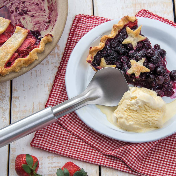 Handcrafted stainless steel ice cream scoop with a stub-nose end resting beside a slice of star-topped berry pie and melting vanilla ice cream on a white plate, featured in Kitchen & Food, Specialty Equipment, Making Ice Cream, Storage and Serving, USA Made, and Best Sellers collections.
