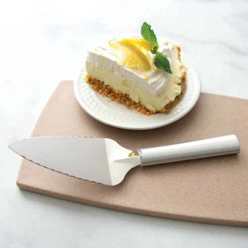Handcrafted serrated pie server with a smooth metal handle resting on a neutral cutting board beside a slice of lemon cream pie garnished with whipped cream and mint, perfect for Kitchen & Food, Storage and Serving, USA Made, Best Sellers, and Promo Eligible collections.