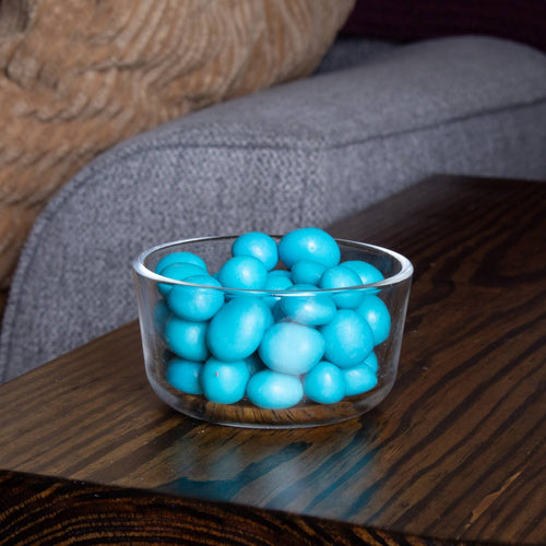 Small clear bowl filled with bright blue coated chocolate-covered blueberries on a dark wooden surface, showcasing a handcrafted treat ideal for Kitchen & Food and Snacks and Sweets collections.