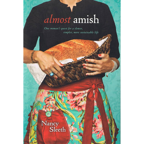 Cover of a handcrafted paperback book showing a woman holding a woven basket with fresh bread, featuring a floral apron and promoting a simpler, sustainable lifestyle, part of Toys, Books & Games, Heritage and Lifestyle Books, and Best Sellers collections.