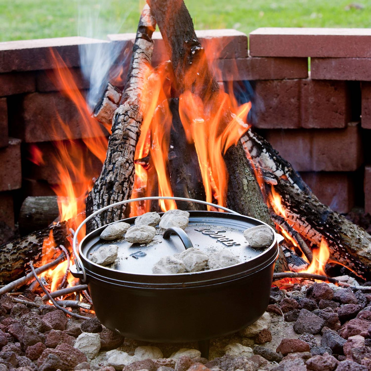 Handcrafted cast iron camp Dutch oven with built-in legs cooking over an open flame, surrounded by hot coals on a fire pit; featured in Farm, Garden & Tool, Camping, Cast Iron, USA Made, and Best Sellers collections.
