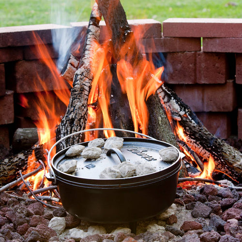 Handcrafted cast iron camp Dutch oven with built-in legs cooking over an open flame, surrounded by hot coals on a fire pit; featured in Farm, Garden & Tool, Camping, Cast Iron, USA Made, and Best Sellers collections.